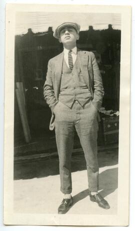 Unidentified young man in three piece suit with newboy cap, hands in pocket, looking from under the brim of the hat directly at the camera.